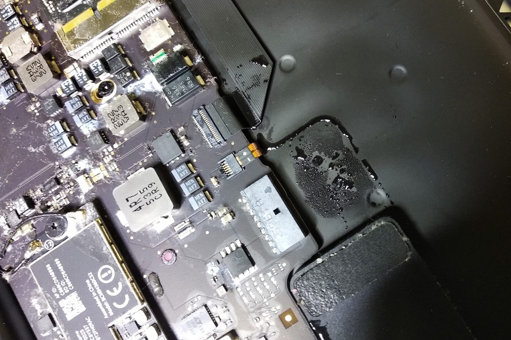 MacBook po zalaniu kawą – widoczne ślady cieczy na płycie głównej i wewnątrz obudowy